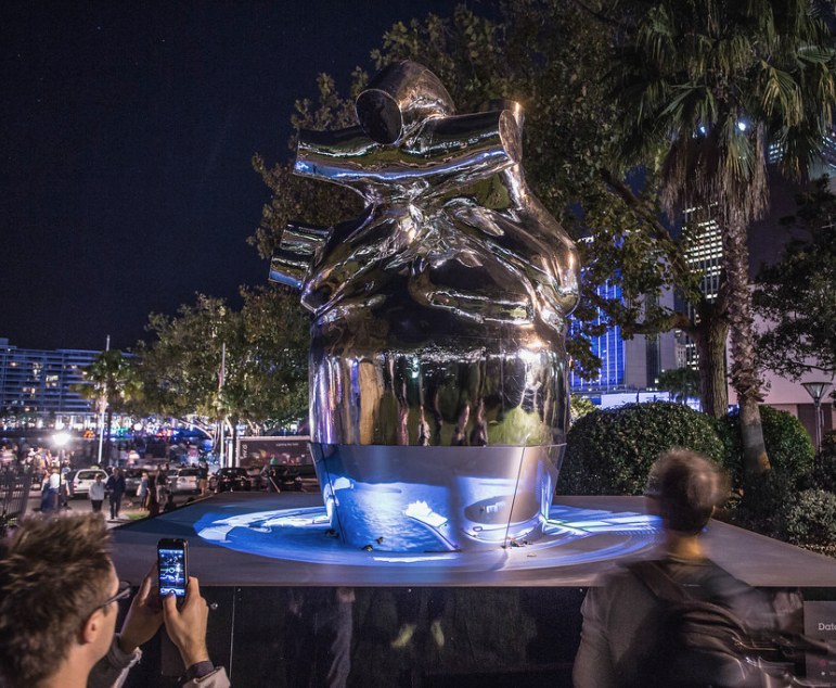 The mirror-polished Heart of the City sculpture glowing at night in Circular Quay, a visitor photographing it