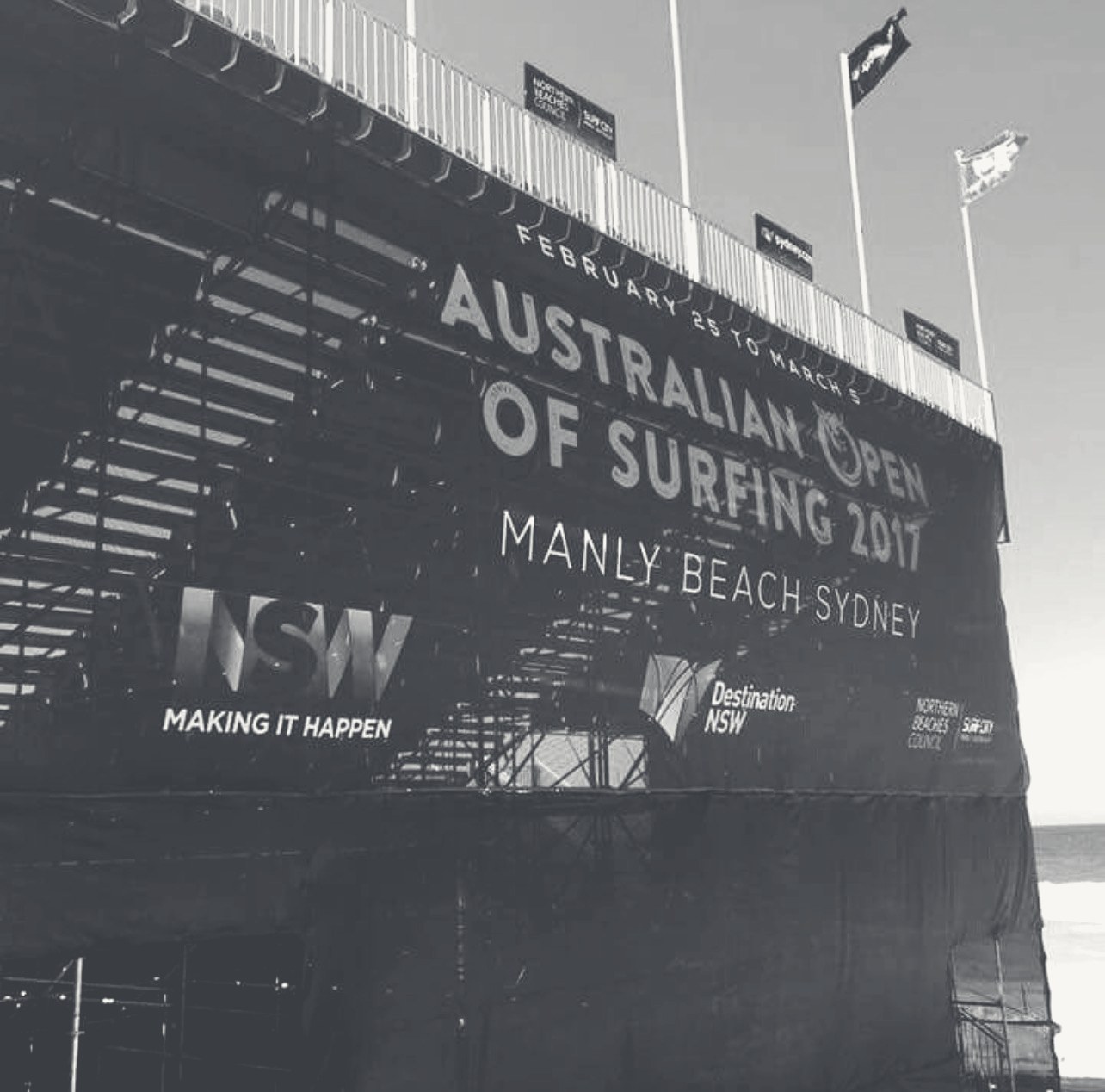 The Australian Open of Surfing broadcast grandstand rising over Manly Beach, graphite monochrome